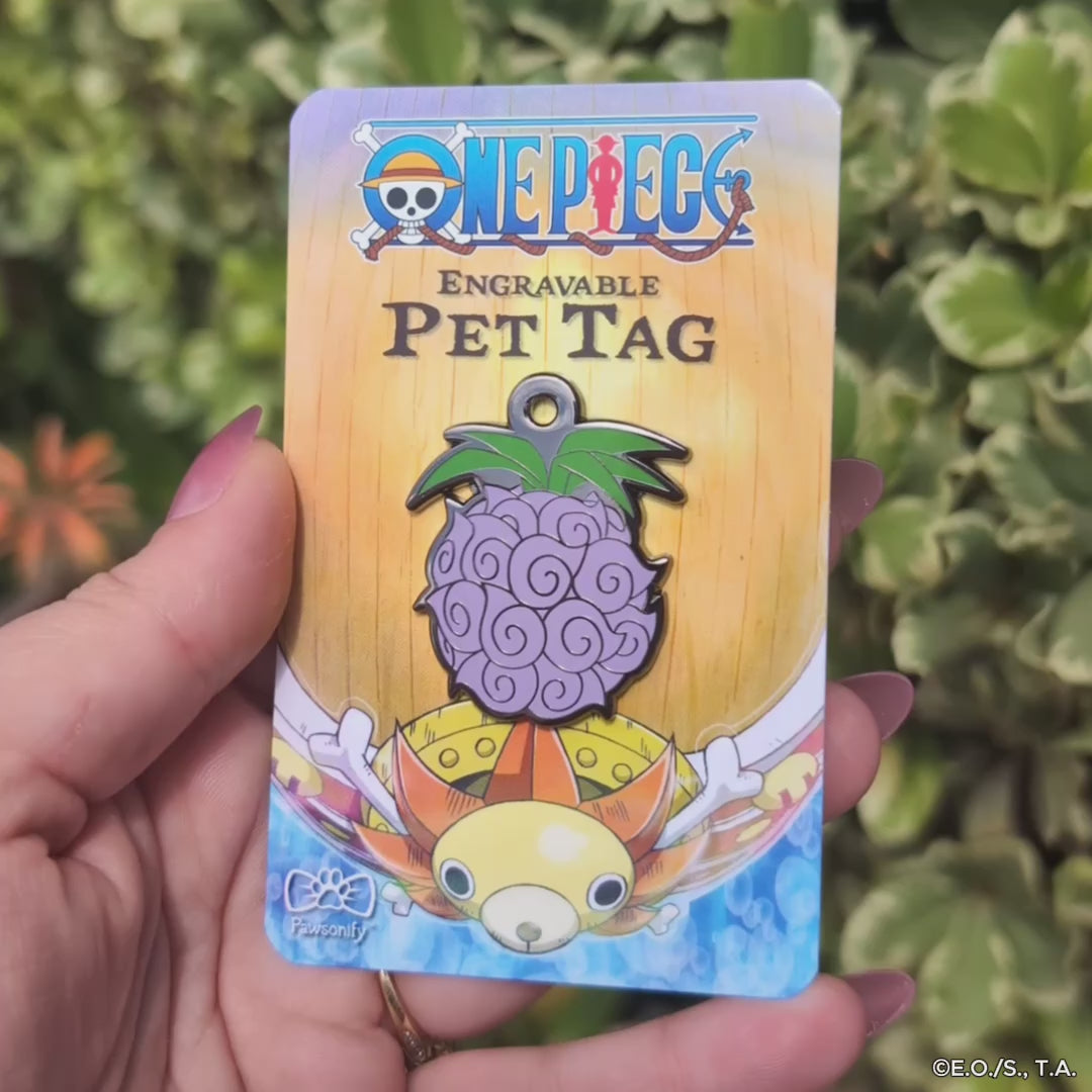 One Piece engravable pet tag featuring the Dark-Dark Fruit design, with a deep purple-black color and swirling patterns, shaped like a clustered spherical fruit with a green stem, displayed on themed backing with the One Piece logo.